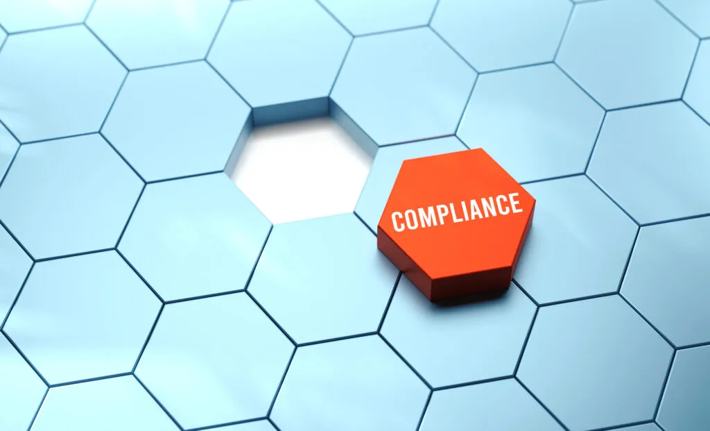 Czerwona kostka z napisem Compliance wśród niebieskich sześciokątnych elementów – ilustracja do sekcji compliance i ładu korporacyjnego w kancelarii KRK